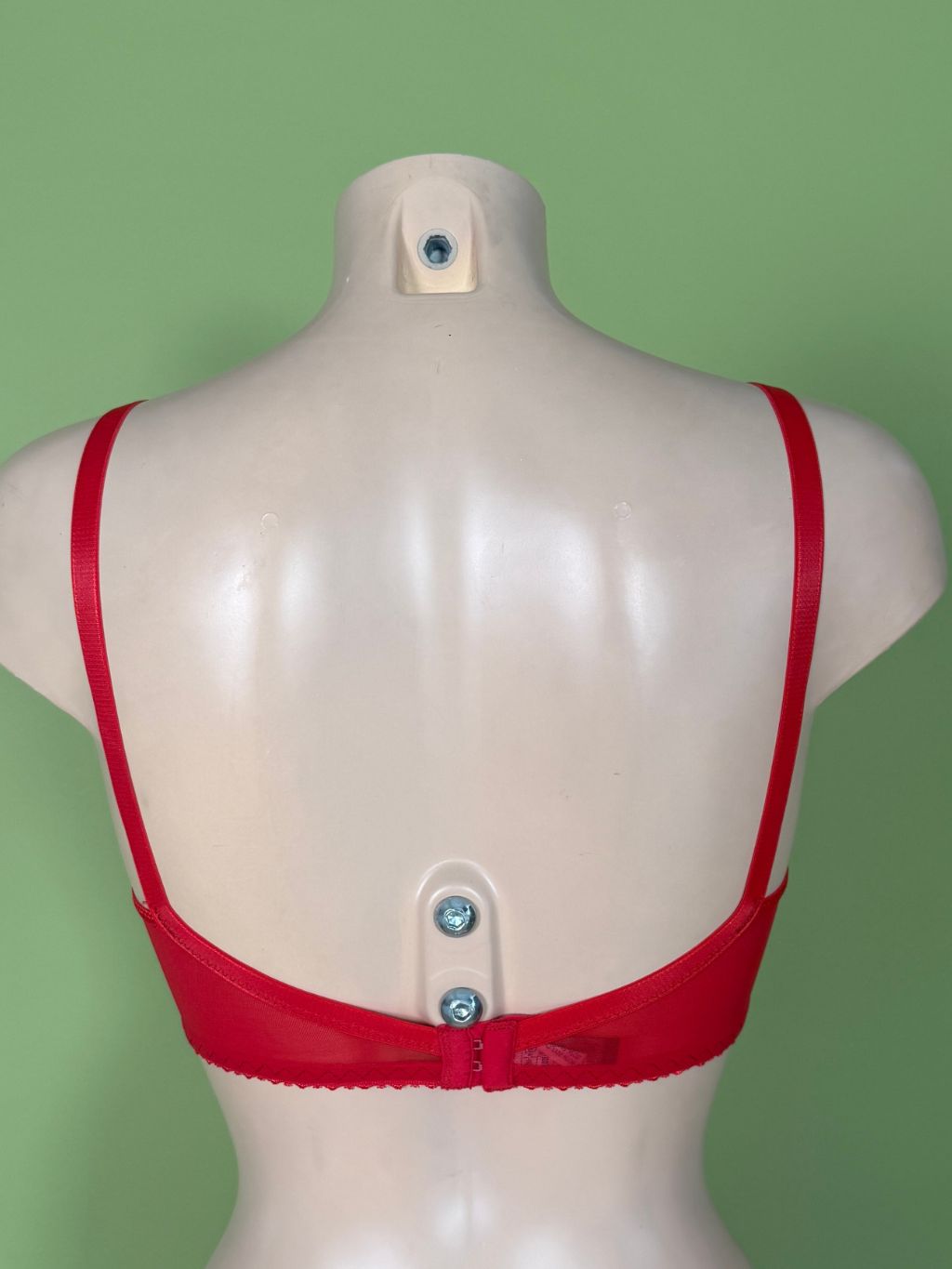 Red soft cup bra shown from the back on a beige mannequin torso against a solid green background.