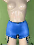 Blue satin high-waisted briefs with black trim, garter straps, and a front opening, displayed on a beige mannequin torso against a green wall.