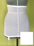 White girdle with garter straps, displayed on a gray dress form against a green background.