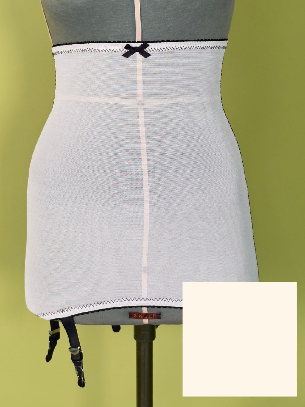 High-waisted cream girdle on a  dress form mannequin against a solid olive green background, with a color swatch overlay in the bottom right corner.