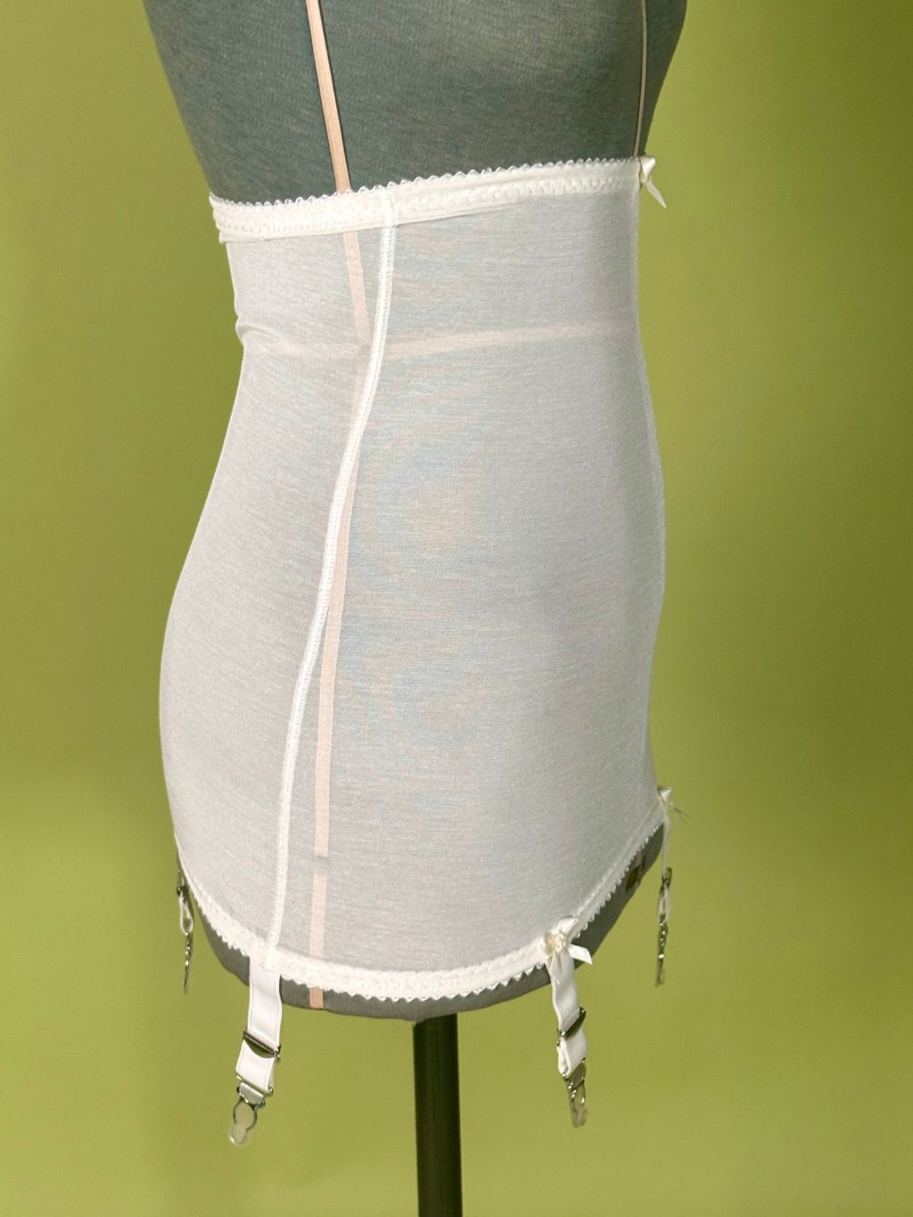 cream high waist girdle with lace trim and adjustable suspender straps, displayed on a gray dress form against a green background.