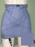 A lavender-blue high-waisted girdle with diagonal zigzag stitching, a black lace-up bow at the waistband, and garter straps on the hips, shown on a mannequin against a light green wall.
