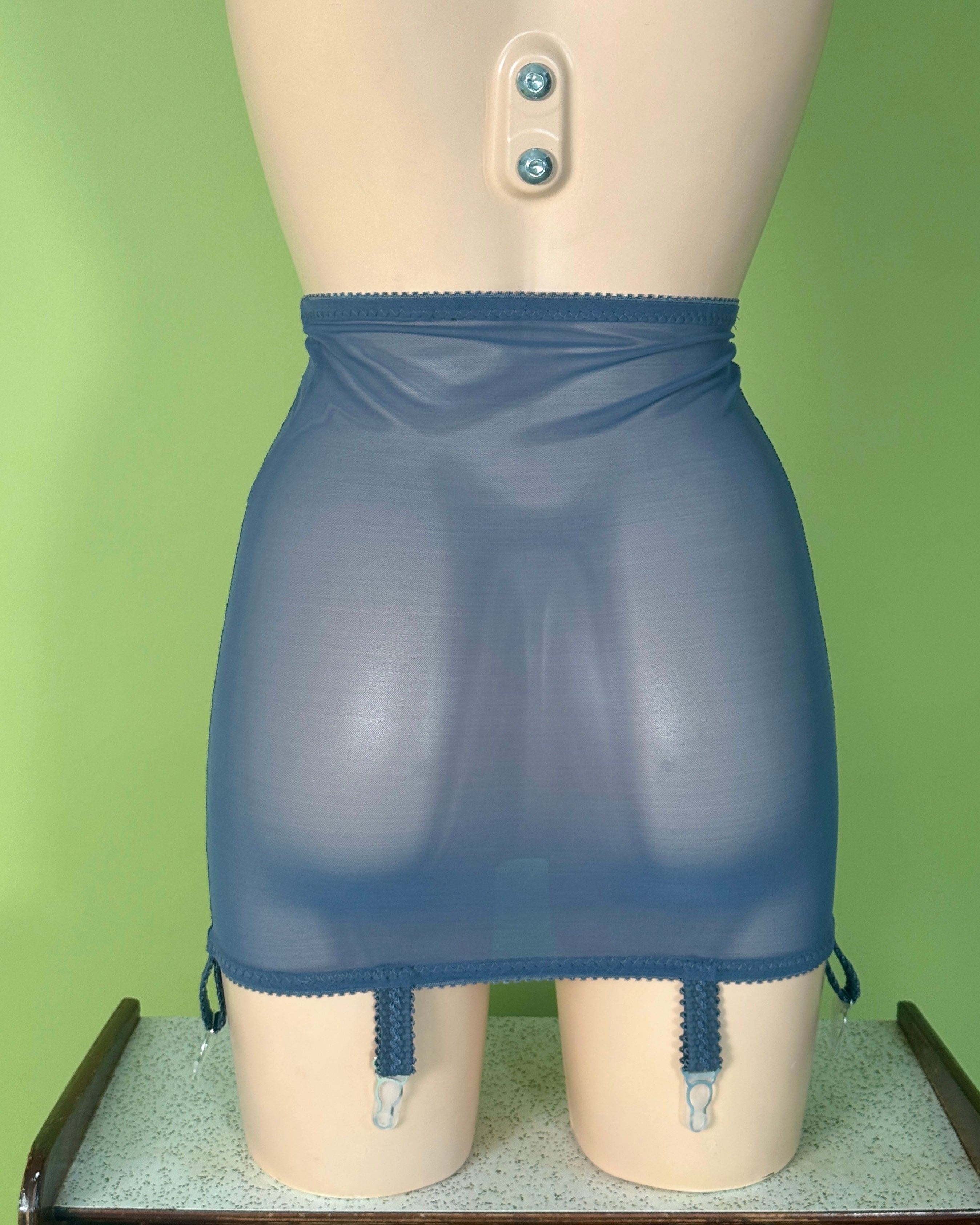 A blue sheer mesh girdle with elastic waistband and leg straps, displayed on a beige mannequin against a light green background.