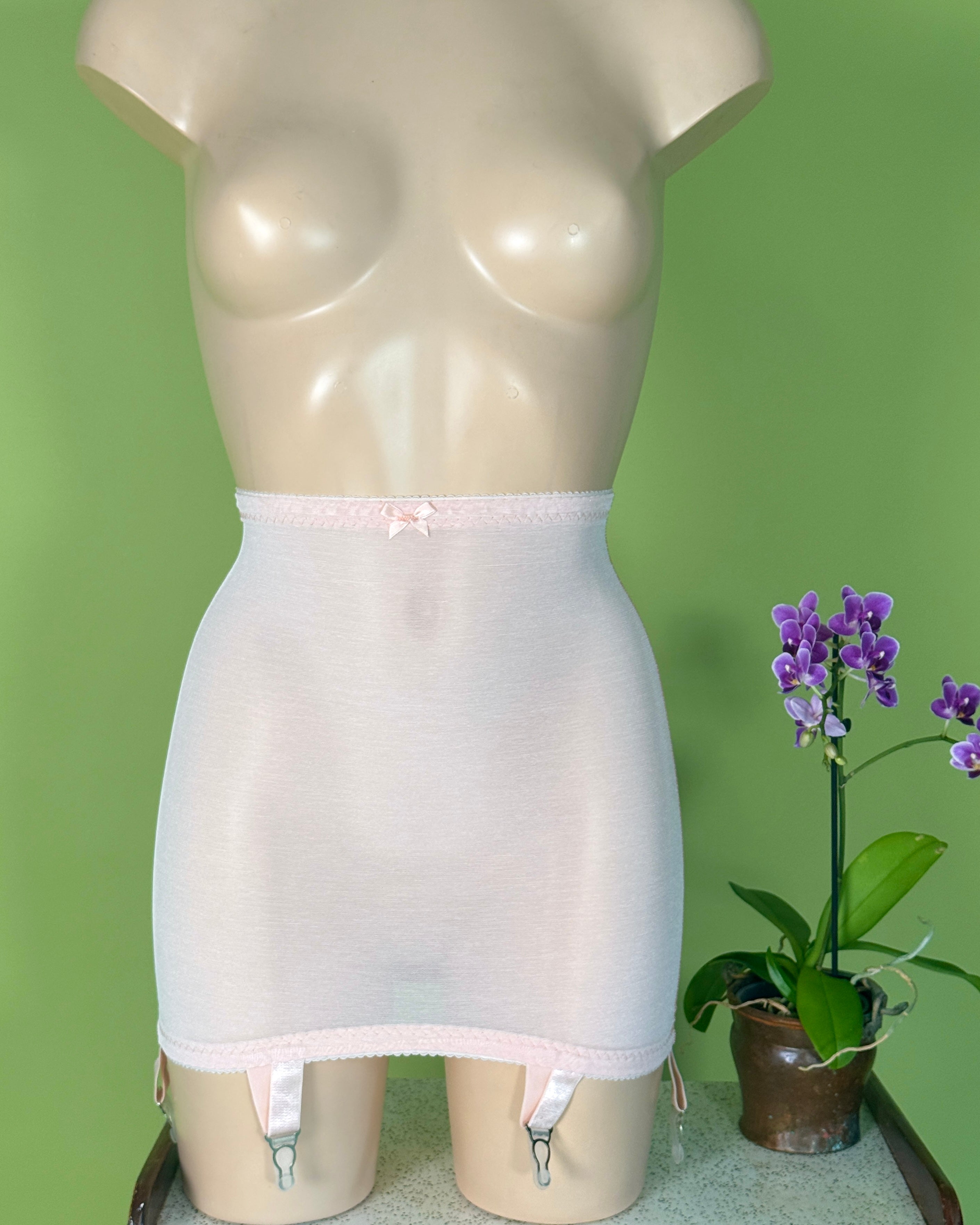A mdisplay a light pink sheer girdle with a small bow at the waistband and attached garter straps. 