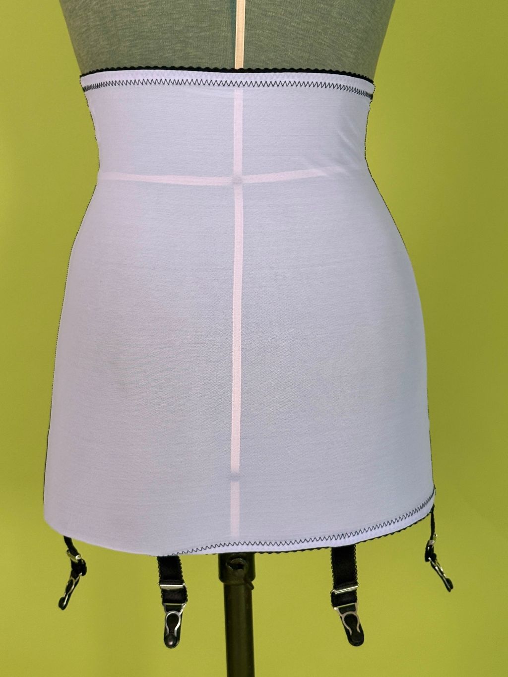 Light purple girdle  with black clips, displayed on a dress form against a yellow-green background.