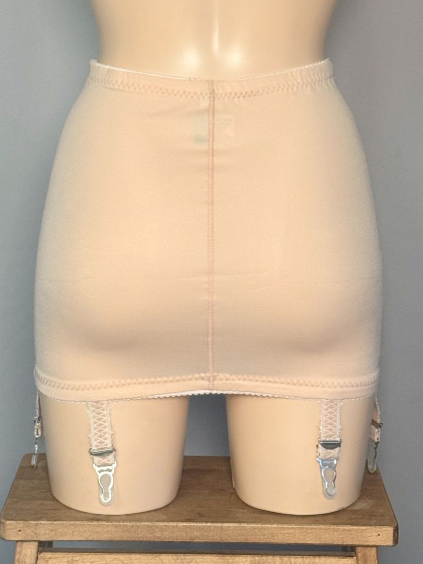 Beige open bottom girdle with silver metal garter clips, displayed on a mannequin torso over a wooden stool.