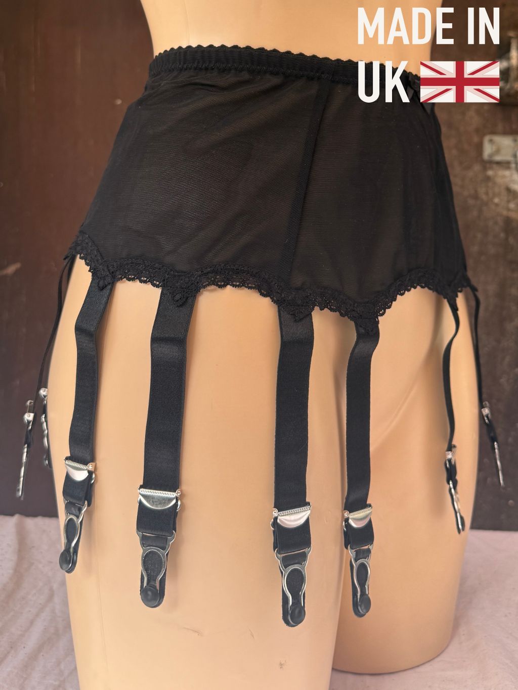 Black garter belt with lace trim and 10 adjustable suspenders with metal clips, displayed on a mannequin. A 'MADE IN UK' graphic with a Union Jack flag is in the top right corner.