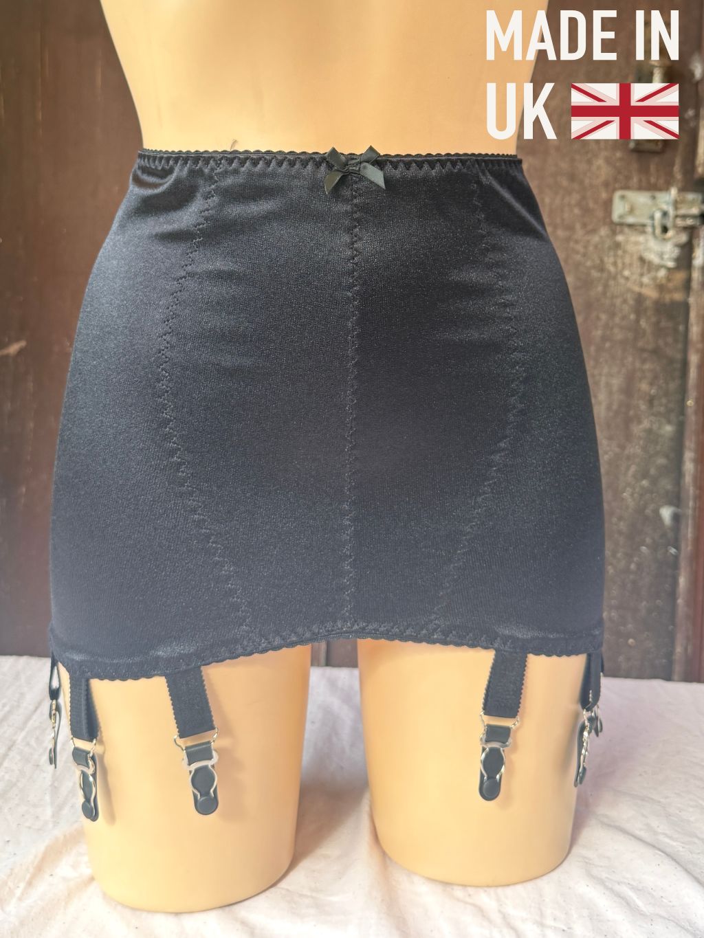 Black girdle with suspenders displayed on a beige mannequin torso, with a 'MADE IN UK' text overlay in the top right corner.
