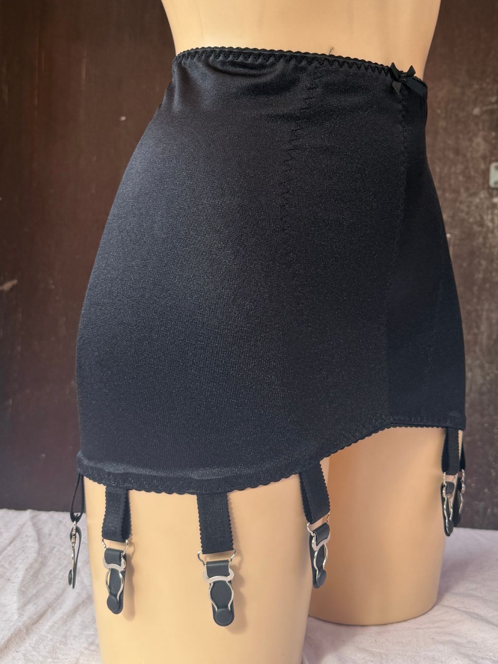 Black girdle with four adjustable suspender straps and metal clips, displayed on a mannequin torso.