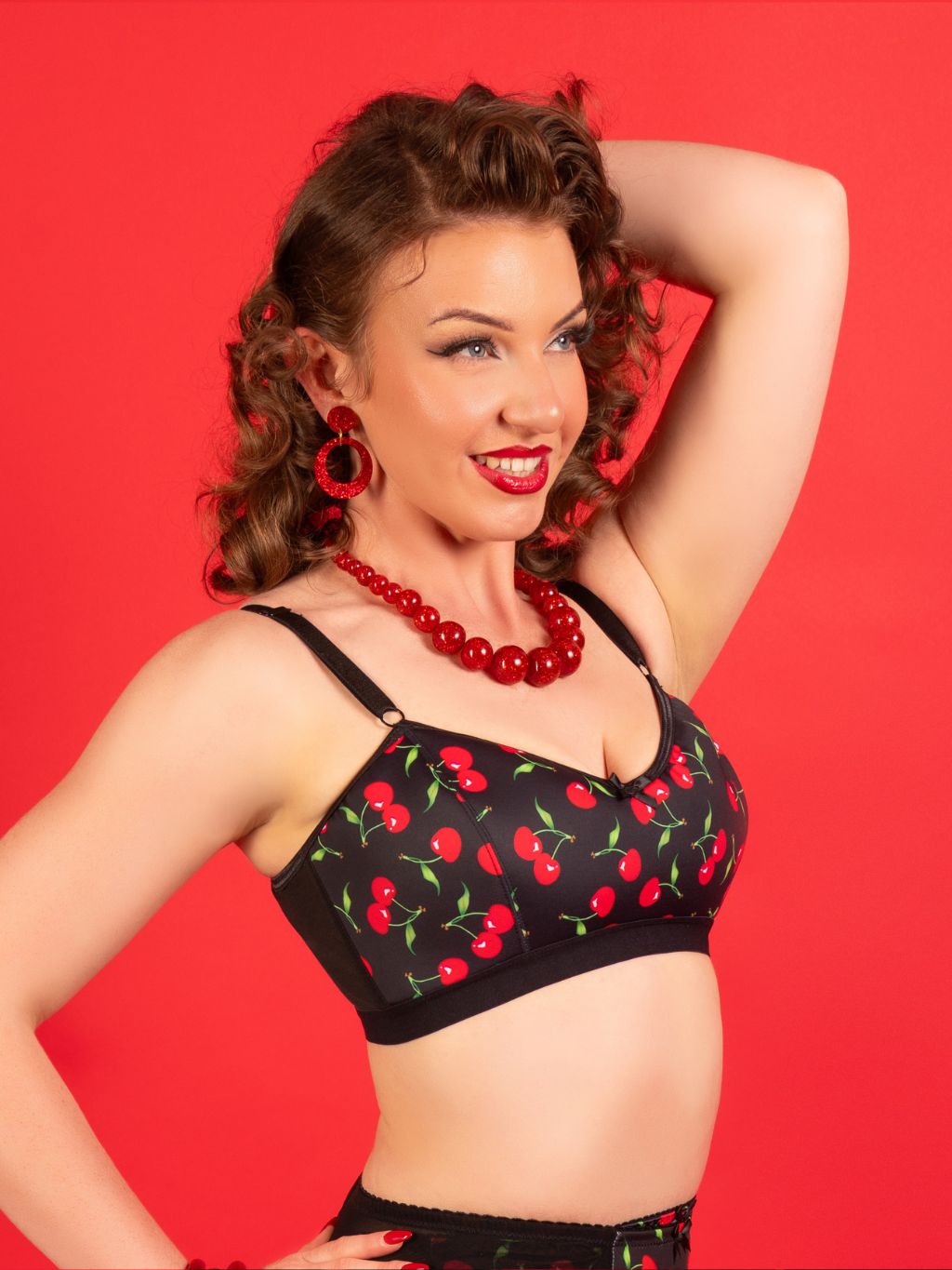 Woman wearing a black bralette with red cherry pattern against a red background