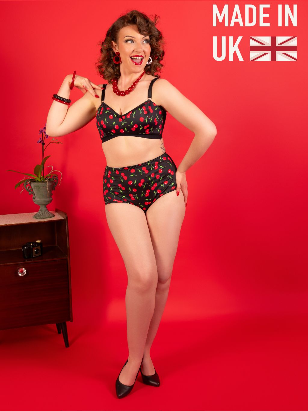 Woman wearing a black and red patterned lingerie set on a red background with 'Made in UK' text.