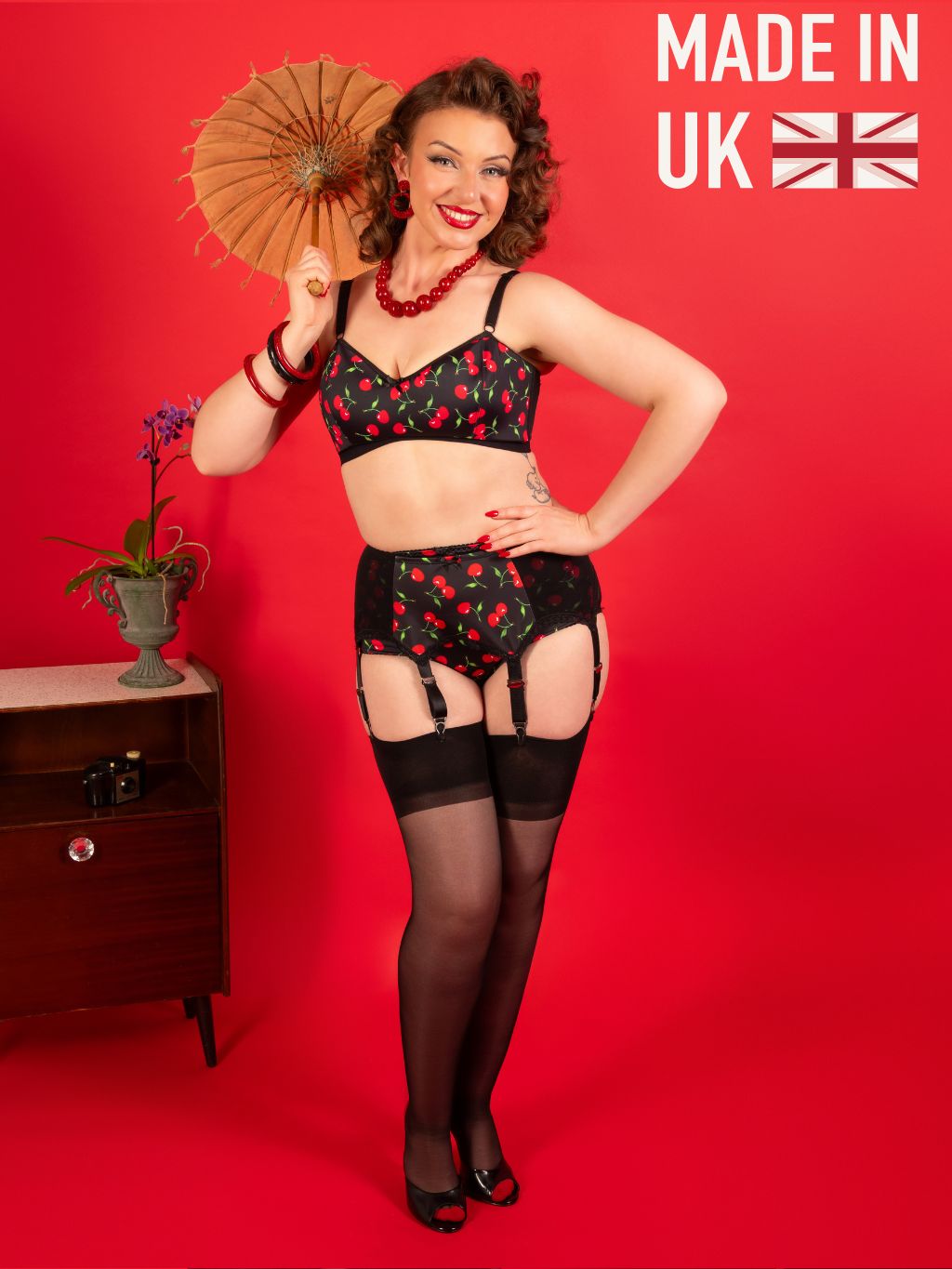 Woman in vintage-style lingerie holding a parasol against a red background with 'Made in UK' text.