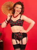 Woman in a black lingerie set with red cherries holding a fan against a red background