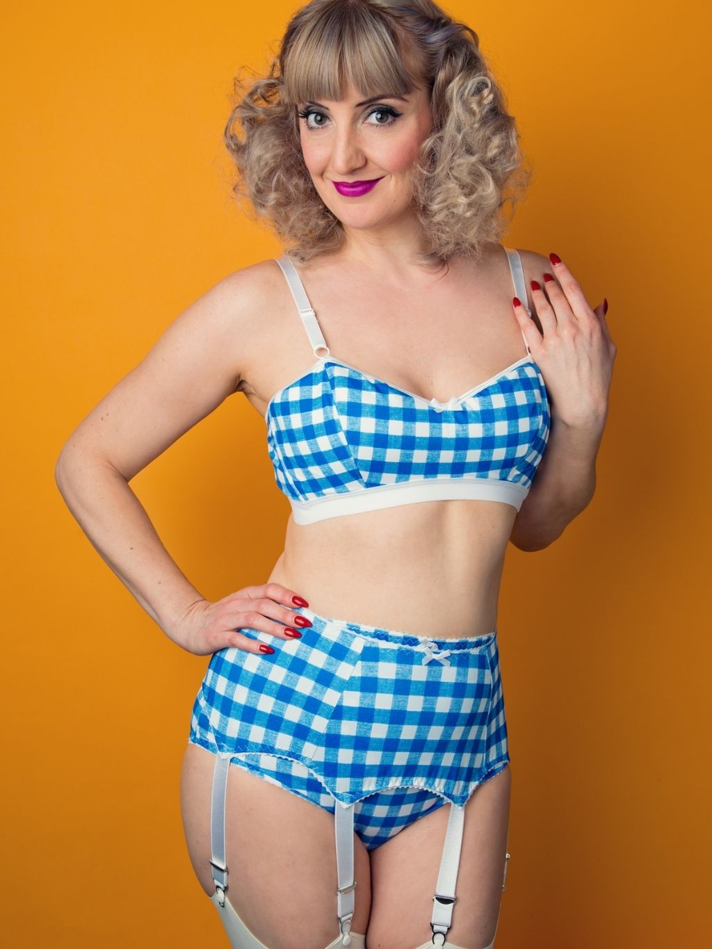 Woman wearing blue and white checkered lingerie with suspenders against an orange background