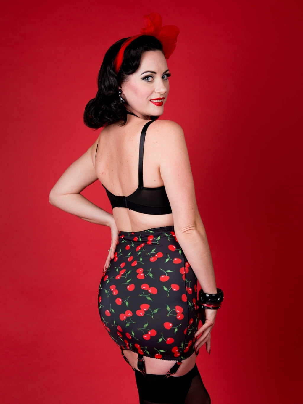 Woman wearing a black cherry-patterned girdle and black top against a red background
