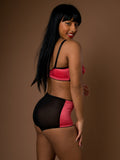 Woman wearing a coral and black lingerie set against a brown background