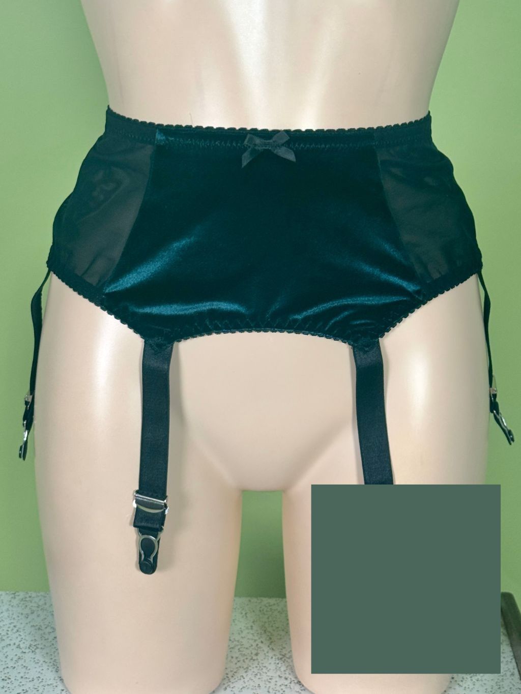 green sheer mesh and velvet garter belt with attached garter straps, displayed on a beige mannequin torso against a light green background.