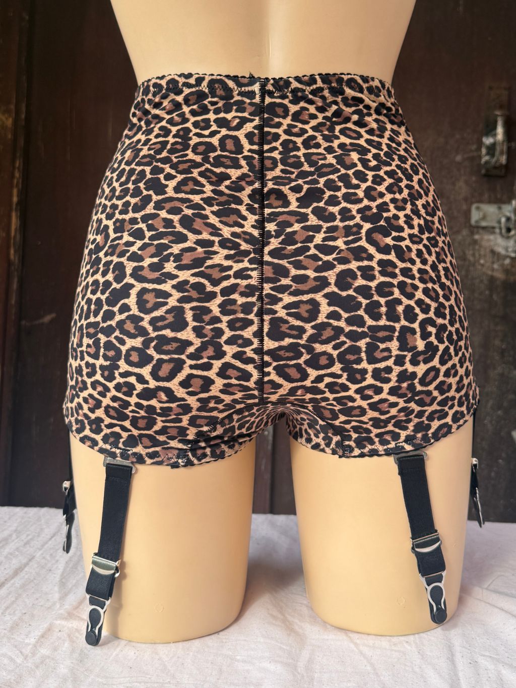 High-waisted leopard print panty girdle  displayed on a beige mannequin, showing the back view with attached black suspender straps.