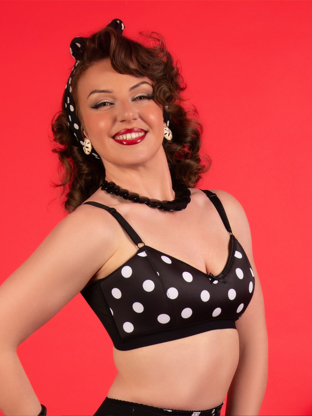 Woman wearing a black polka dot bralette against a red background