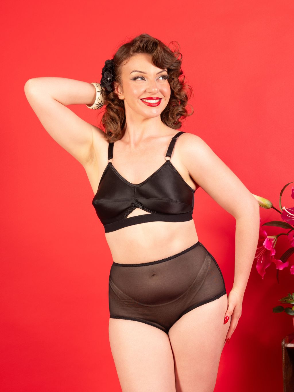 Woman wearing a black bra and brown underwear against a red background
