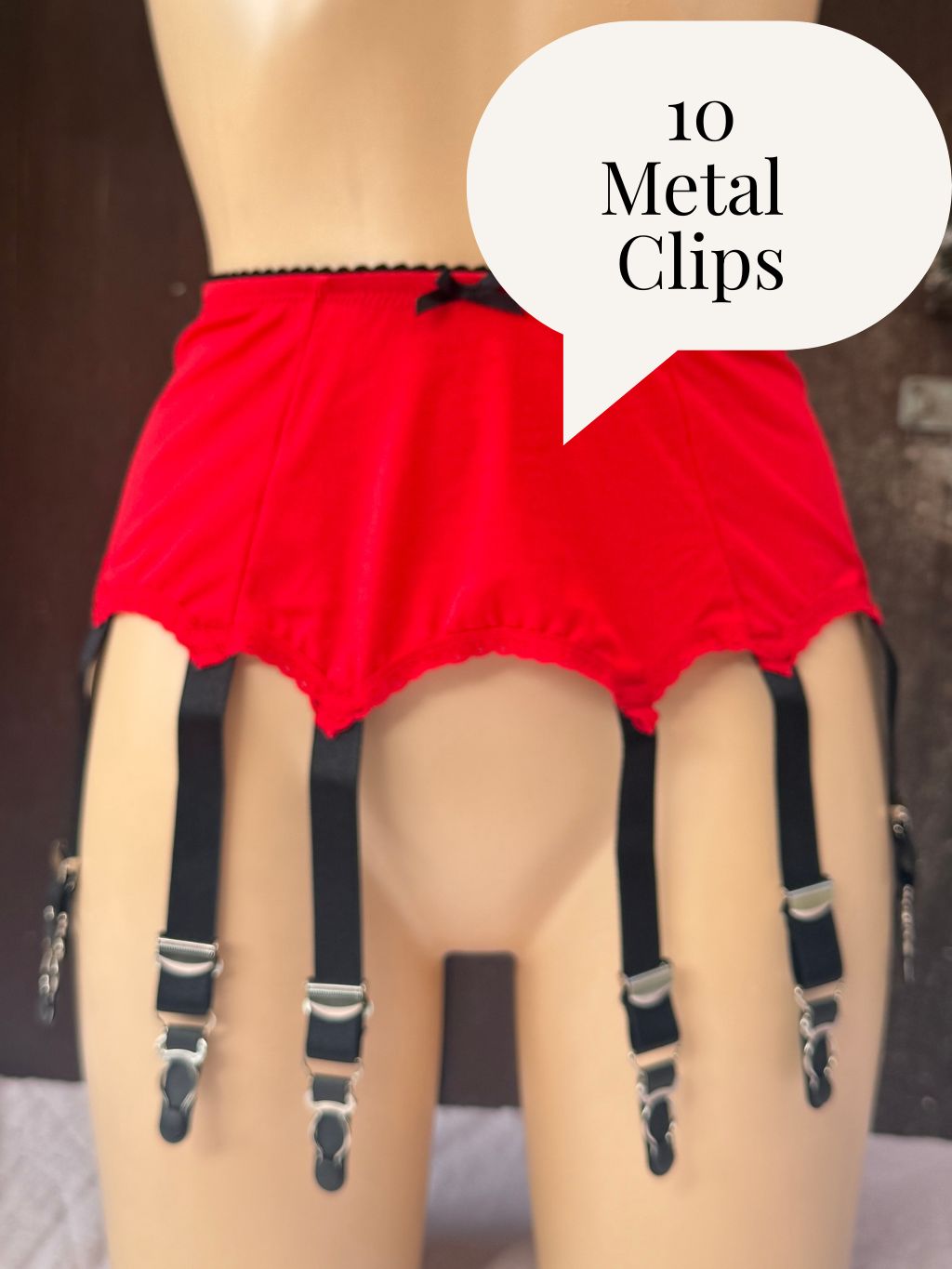Red garter belt with black suspender straps and silver metal clips displayed on a beige mannequin torso, with a speech bubble reading '10 Metal Clips'.