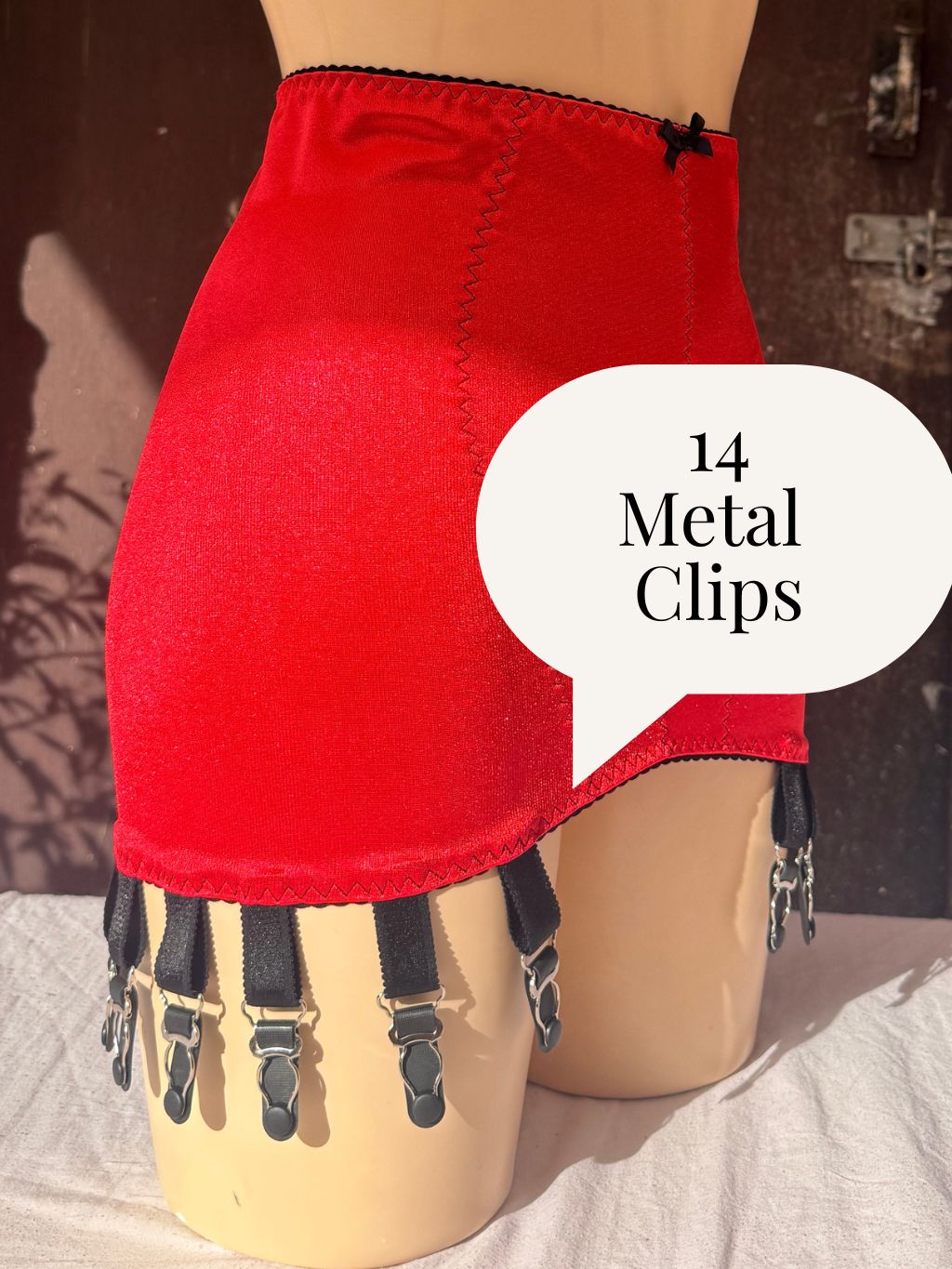 Red high-waisted girdle with black suspenders and 14 metal clips, displayed on a mannequin leg with a speech bubble reading '14 Metal Clips'.