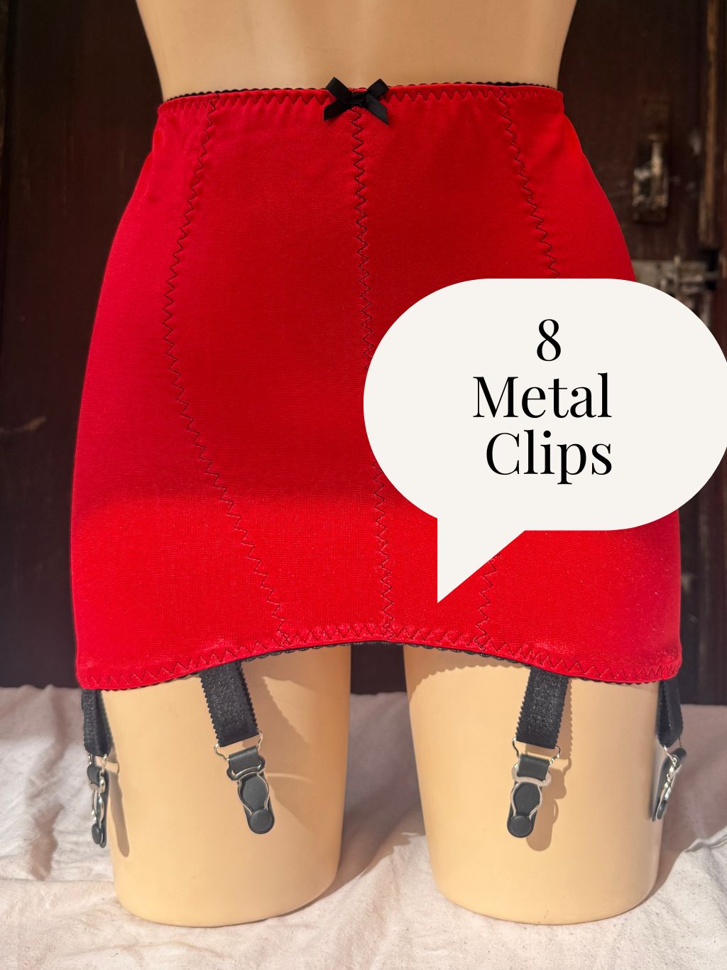 Red girdle with black suspenders displayed on a mannequin, featuring a white speech bubble overlay that reads '8 Metal Clips'.