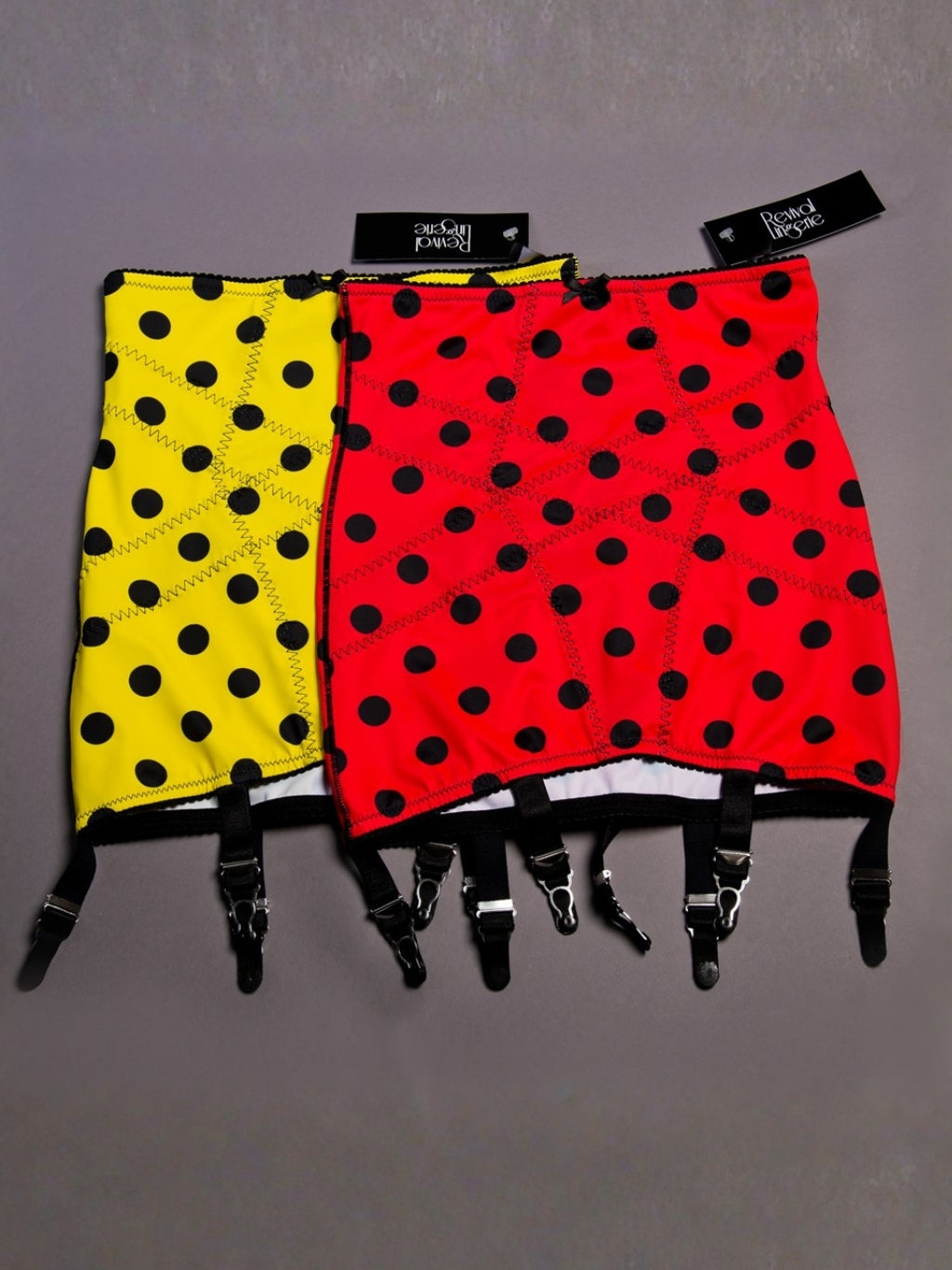 Two pairs of polka dot girdles, one yellow and one red, with black suspenders on a gray background.