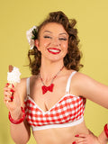 Woman in a red and white checkered bralette holding an ice cream cone against a yellow background