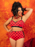 A woman modeling a red and black polka dot two-piece lingerie set against a textured orange background.