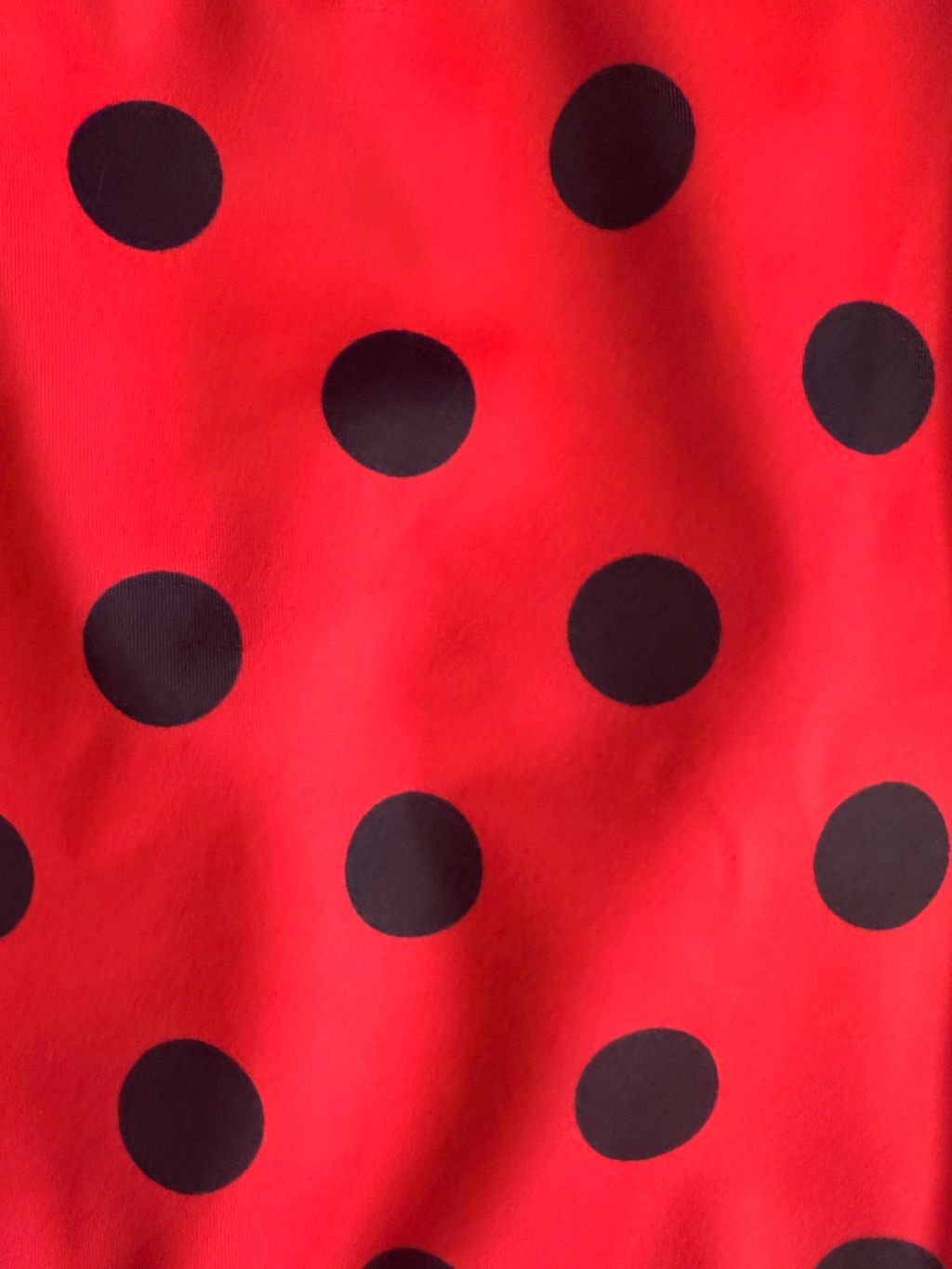 A close-up of a red fabric with a black polka dot pattern, showing the texture and drape of the material.