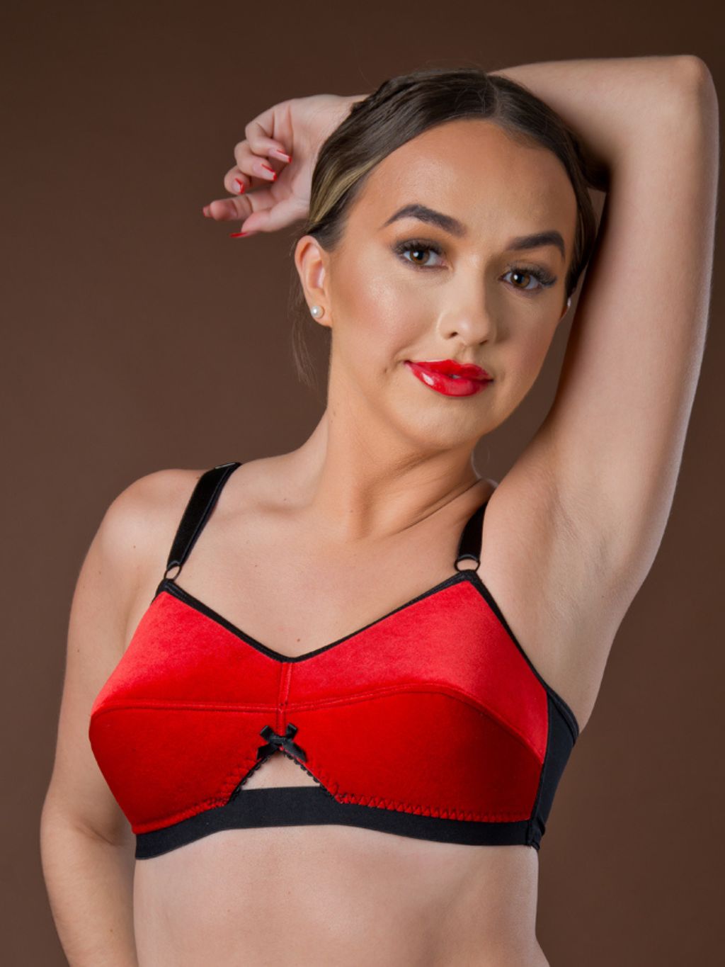 Woman wearing a red velvet bra with black straps against a brown background