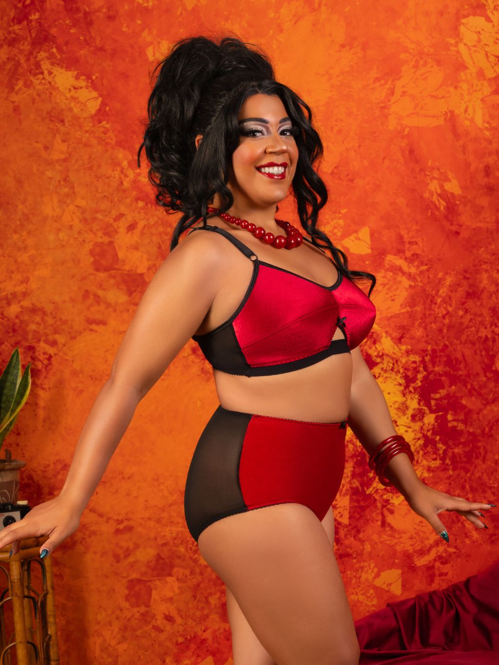 A woman modeling a two-piece lingerie set with a red and black color-blocked design, posing against a textured orange and red background.