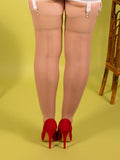 Person wearing beige stockings and red high heels on a yellow background
