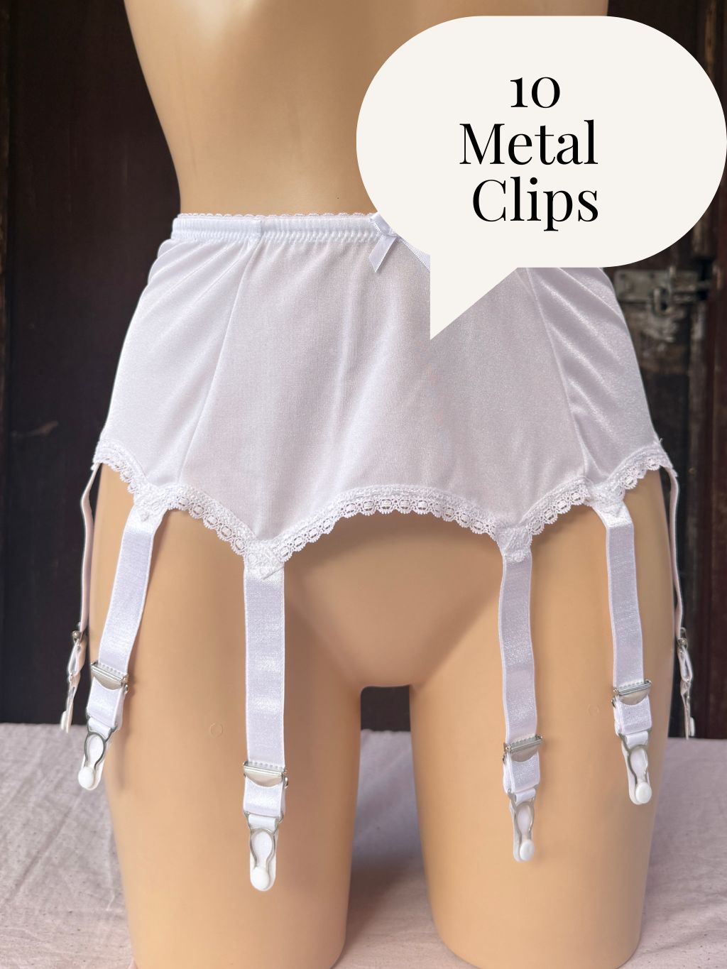 White garter belt with lace trim and 10 metal clips displayed on a mannequin torso, with a speech bubble overlay reading '10 Metal Clips'.