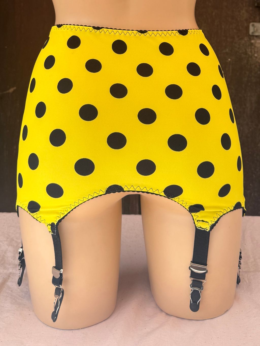 Yellow roll on girdle with black polka dots and attached black garter straps, displayed on a mannequin lower body.