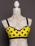 Yellow bra with black polka dots on a mannequin against a lace background